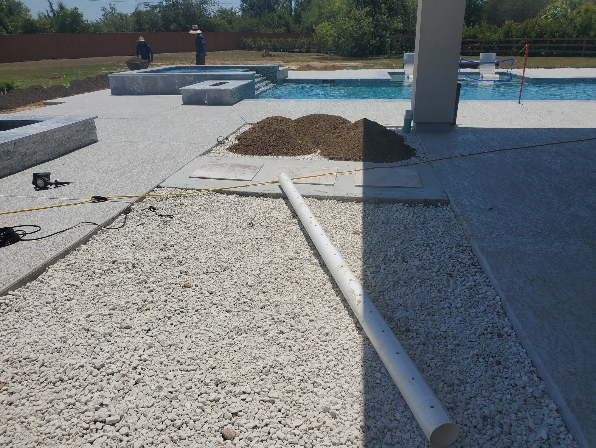 Crushed aggregate base spread over a pool deck sub-grade with a perforated drain line running through it