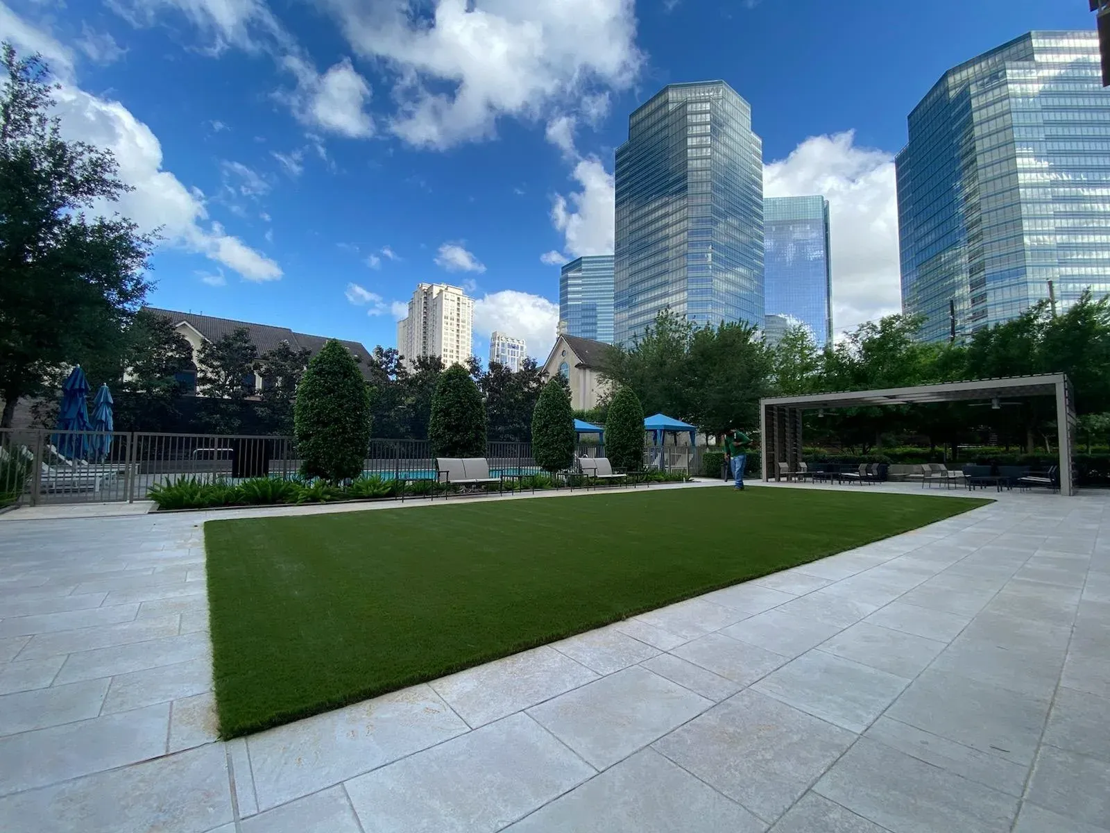A rectangular turf lawn set into a paved plaza, with the Houston skyline rising behind it