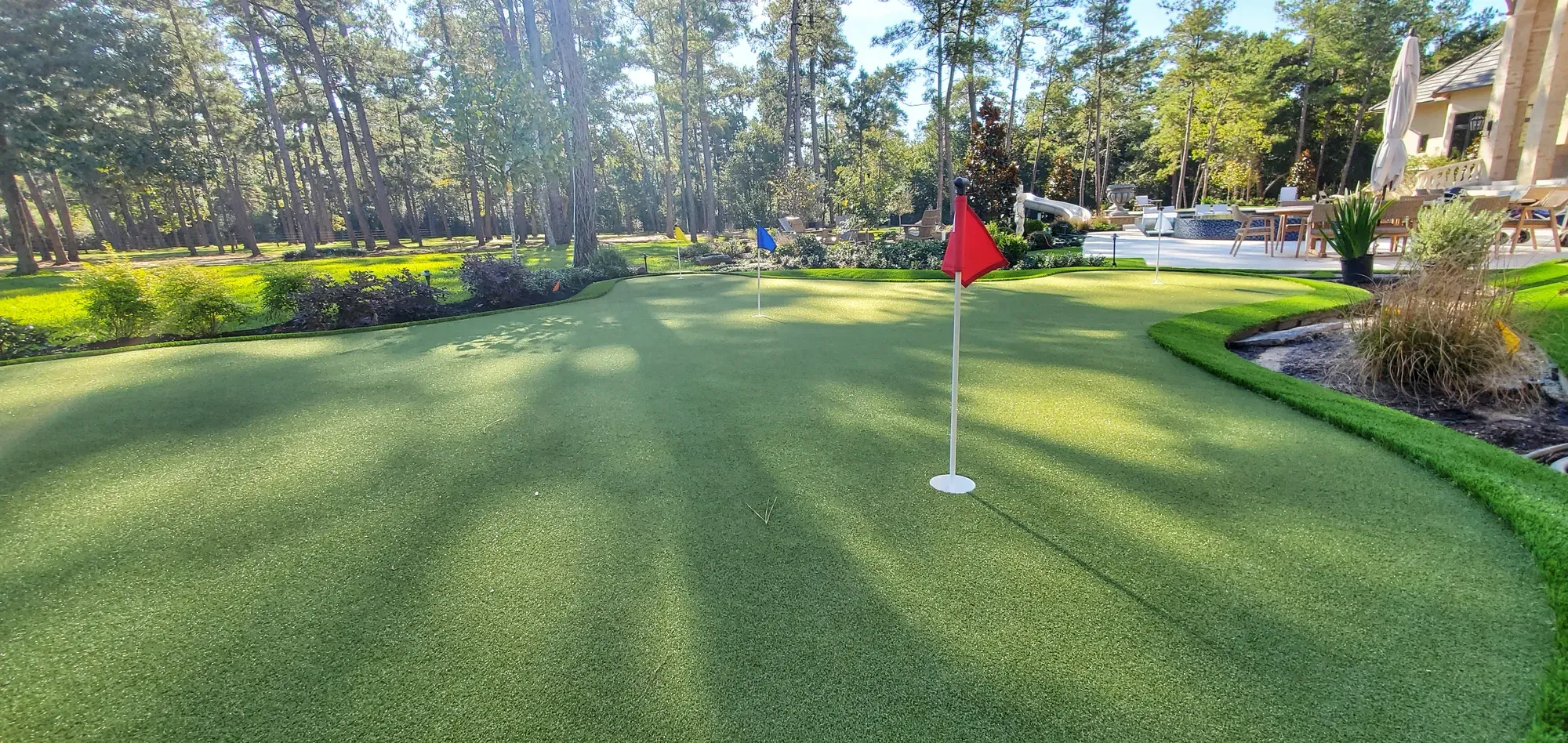 A large contoured practice green with a red flag, framed by planting and trees