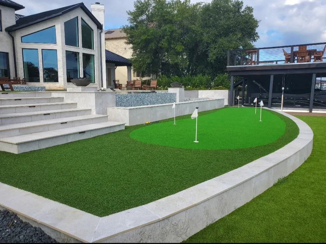 A turf lawn stepping up to a raised putting green with four flags behind a modern Houston home