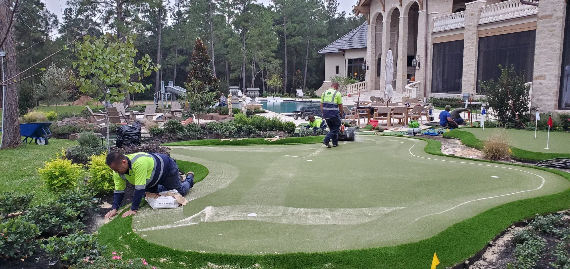Two installers cutting and fitting turf around the curved edge of a new backyard putting green