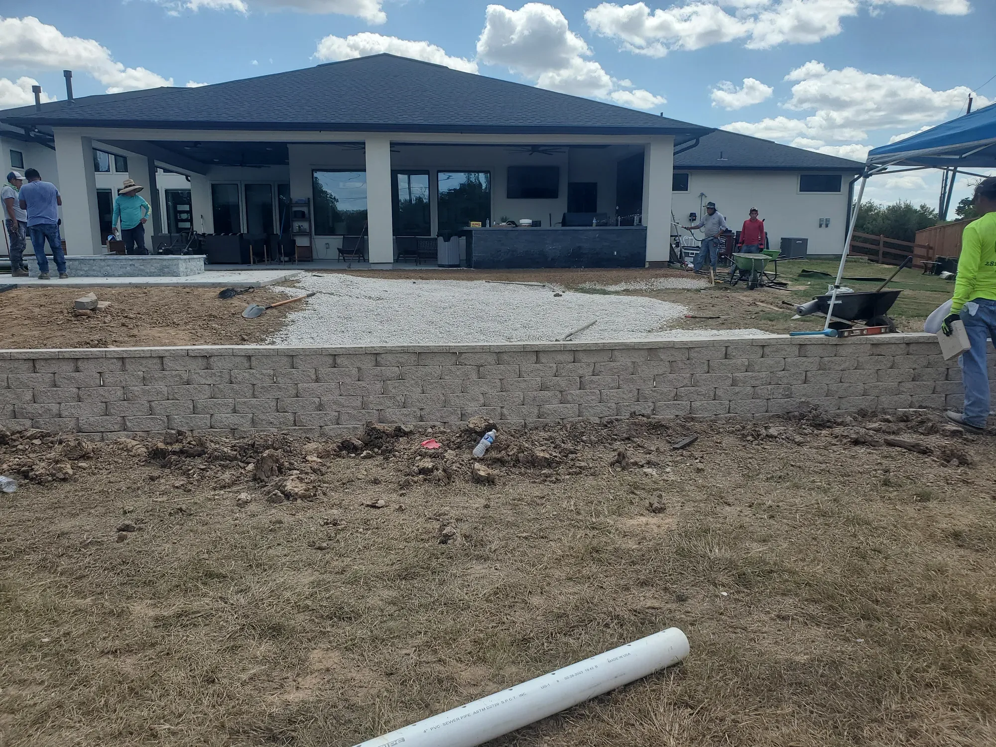 A graded base pad spread flat across a back yard behind a finished block retaining wall