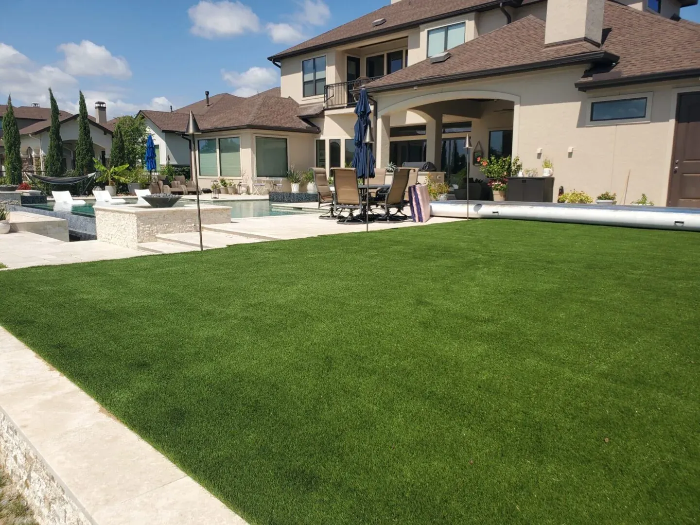 A wide artificial turf lawn behind a large home, running from the pool deck to the property edge